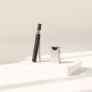 Sleek vape pen and compact pod kit on a neutral surface with soft lighting and gentle vapor wisps rising around them.